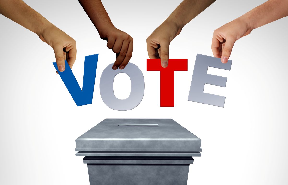 Hands holding letters spelling "VOTE" above a ballot box.