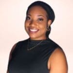 Xavia Francis wearing a black sleeveless top, black headband, and gold necklace is smiling against a plain background.