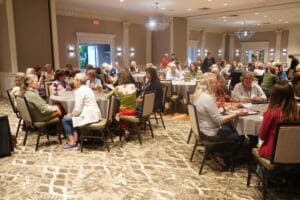 A group of people seated at round tables in a well-lit conference room, engaged in discussion or activities during a meeting or event.