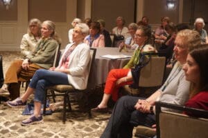 A group of women sit attentively in a conference room, listening to a presentation.